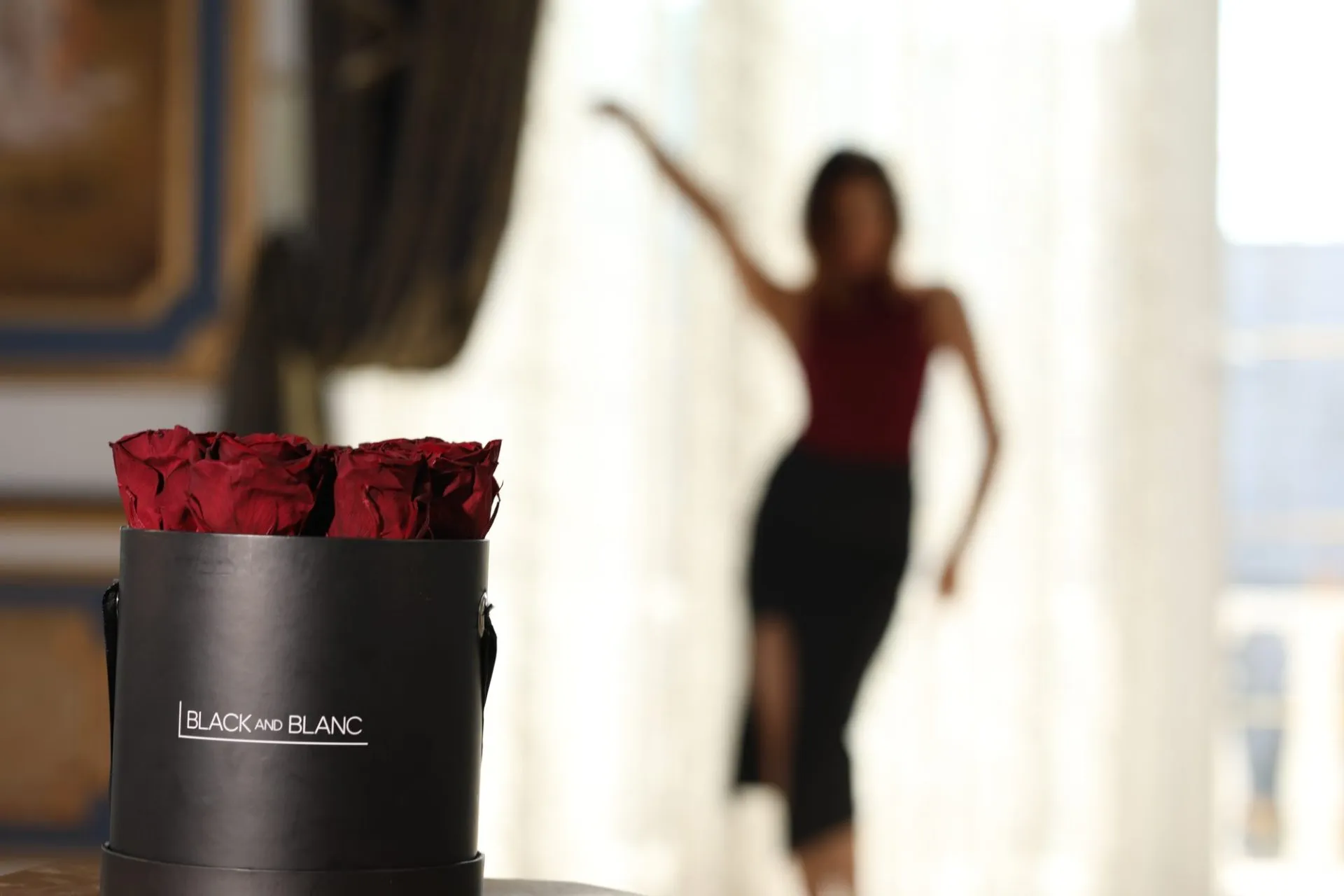 Still from the Black and Blanc Fleur brand film: a black hatbox of red roses with a dancer behind