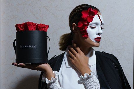 The masked model holds the hatbox out on one hand, eyes closed