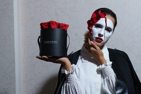 The masked model raises the hatbox beside her face, one hand at her cheek