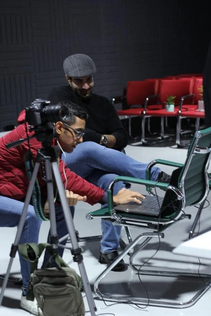 Two crew members review a shot on a laptop beside a camera on a tripod