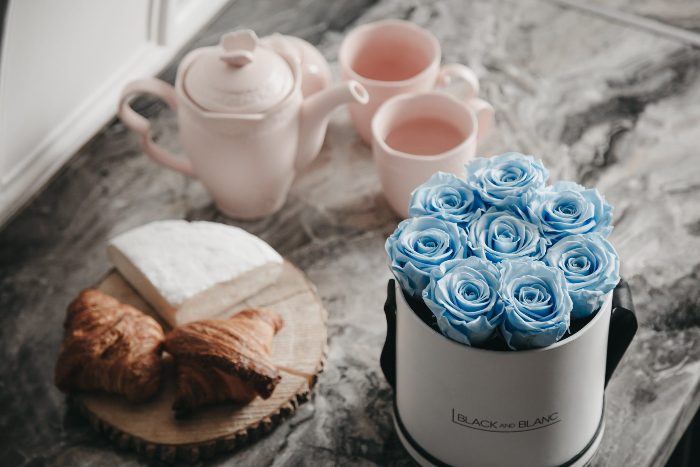 A white hatbox of pale blue roses on a marble breakfast table