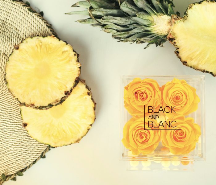 Yellow roses in a clear acrylic box beside sliced pineapple