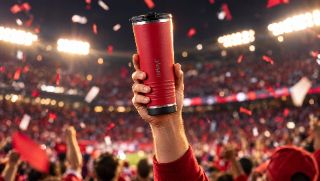 A fan raises the red leHøyt tumbler in a floodlit stadium